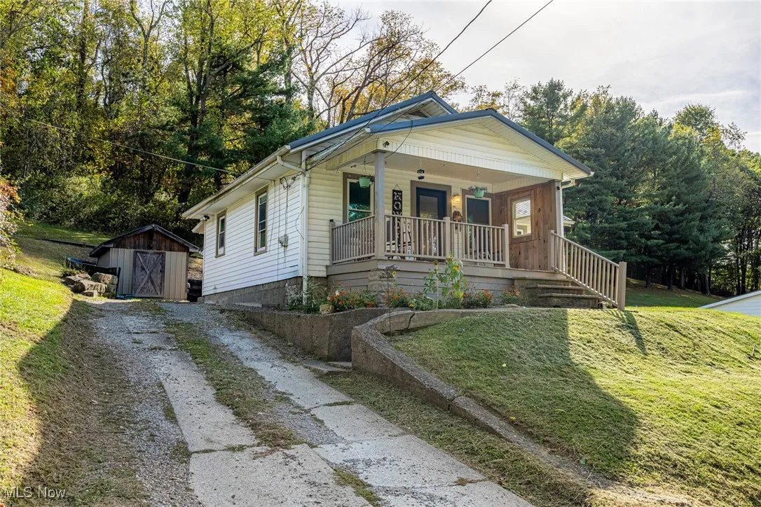 Bungalow-style home featuring covered porch, a front lawn, a storage shed, driveway, and view of scattered trees