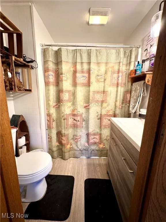 Bathroom featuring vanity, a shower with shower curtain, tile walls, and light wood-style floors