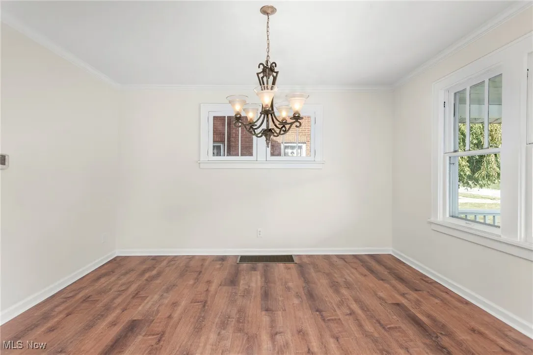 Unfurnished dining area with dark wood finished floors, ornamental molding, and a chandelier
