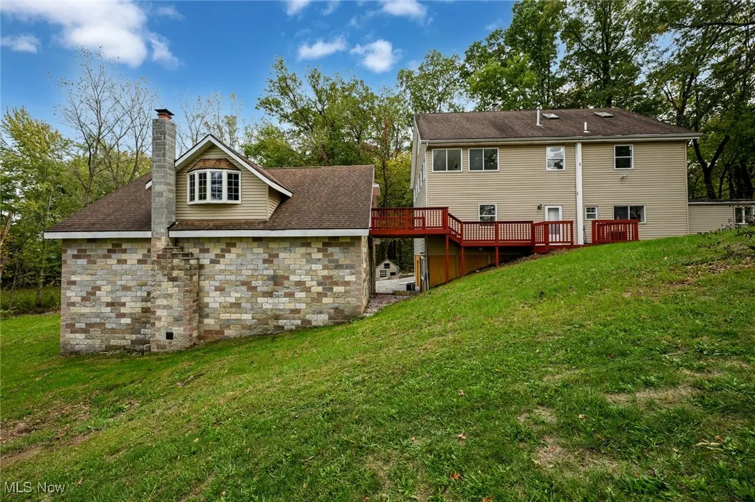 Back of house featuring a lawn, a deck, a chimney, and roof with shingles