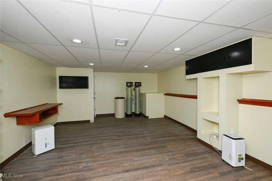 Below grade area with a drop ceiling, dark wood-style flooring, recessed lighting, and a water softener system