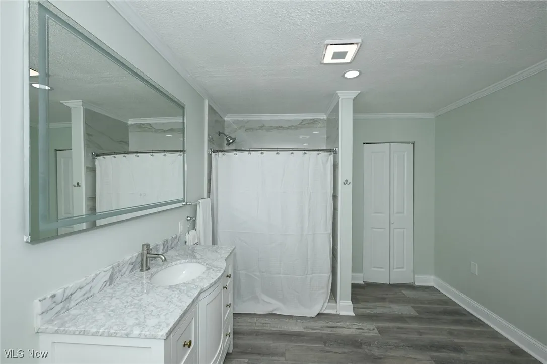 Full bath featuring dark wood-type flooring, a textured ceiling, vanity, crown molding, and a shower with shower curtain