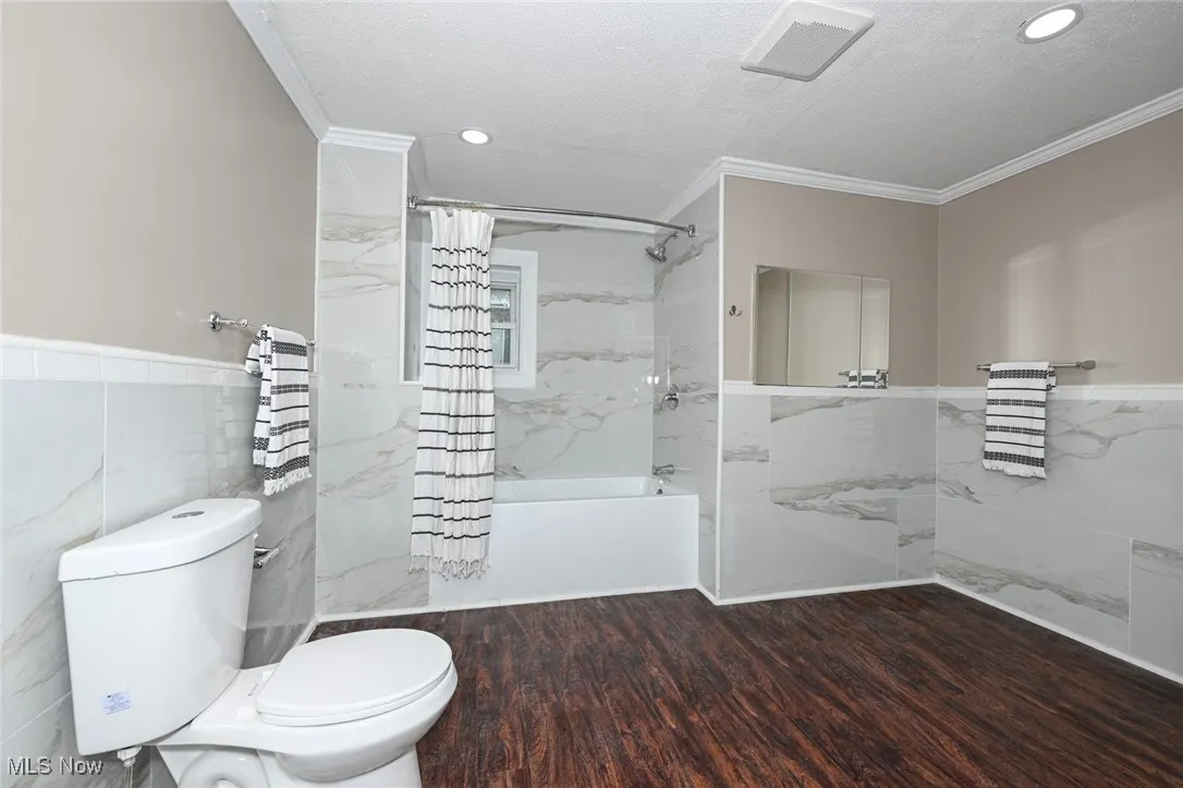 Full bath with tile walls, shower / bath combo, wainscoting, ornamental molding, and a textured ceiling