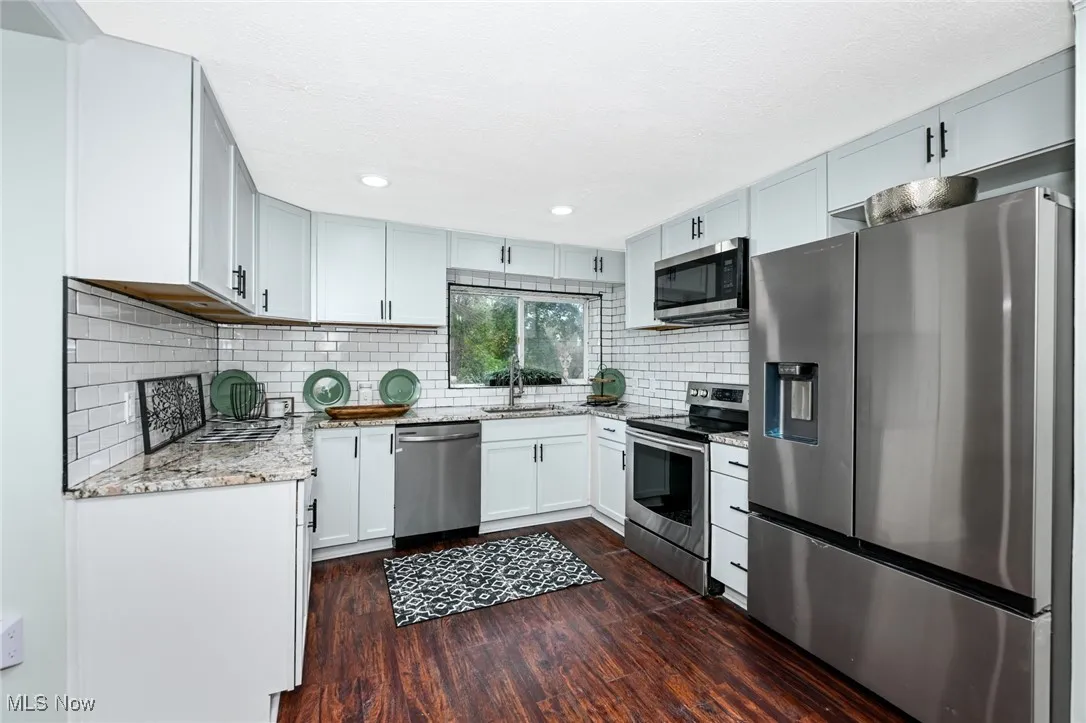Kitchen with appliances with stainless steel finishes, light stone counters, dark wood-style flooring, tasteful backsplash, and recessed lighting