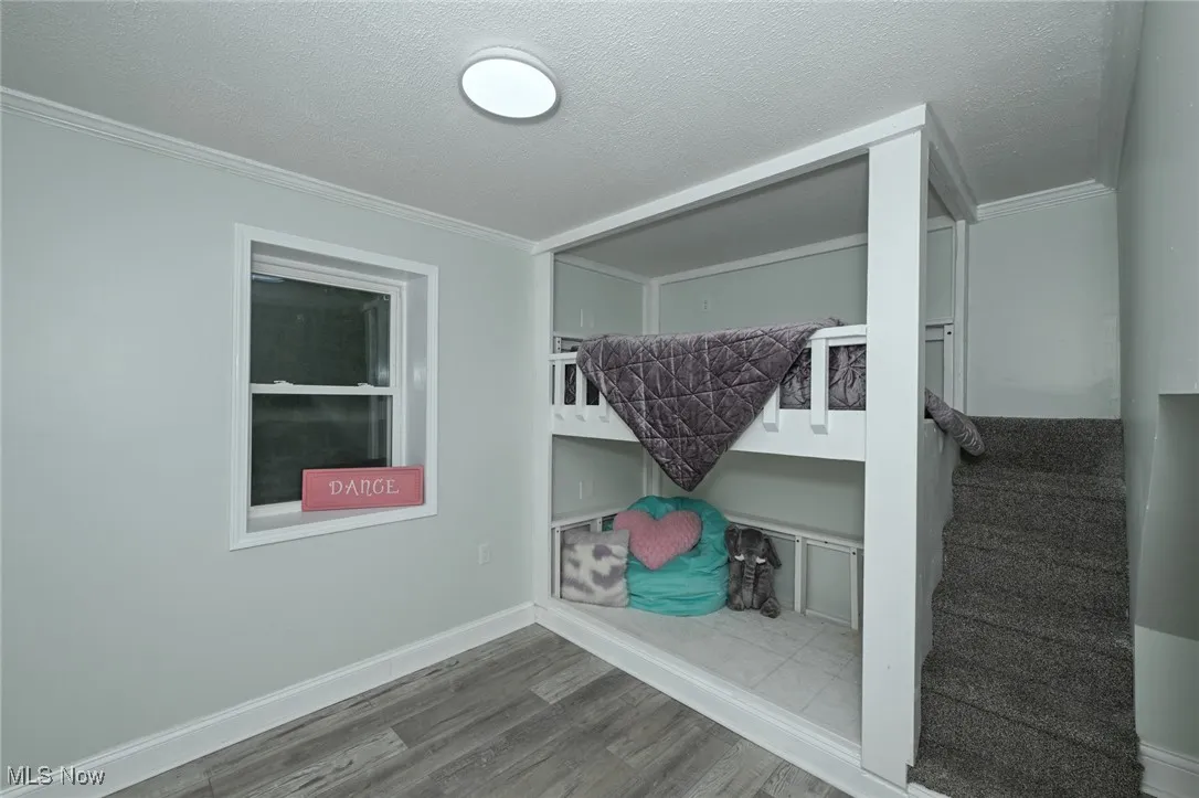Unfurnished bedroom with wood finished floors, a textured ceiling, and crown molding