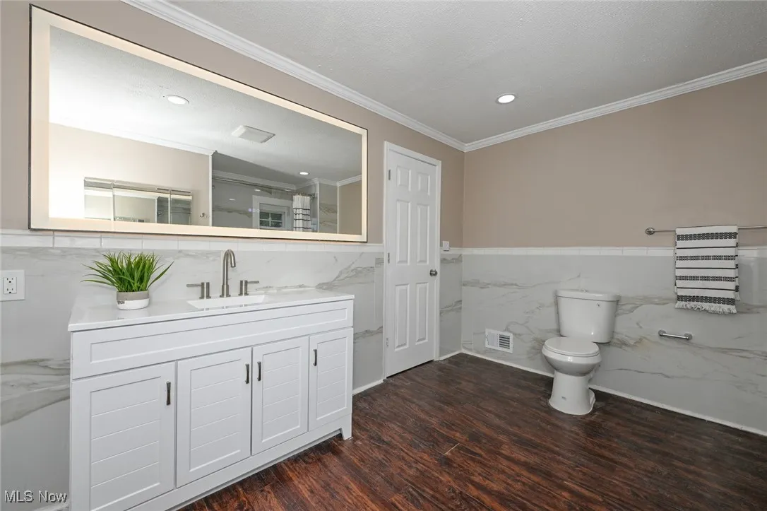 Bathroom featuring vanity, ornamental molding, dark wood-style flooring, recessed lighting, and tile walls