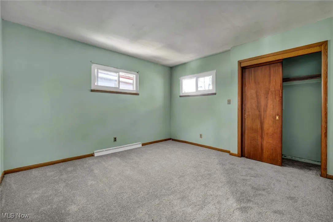 Unfurnished bedroom featuring carpet floors, a closet, and a baseboard heating unit