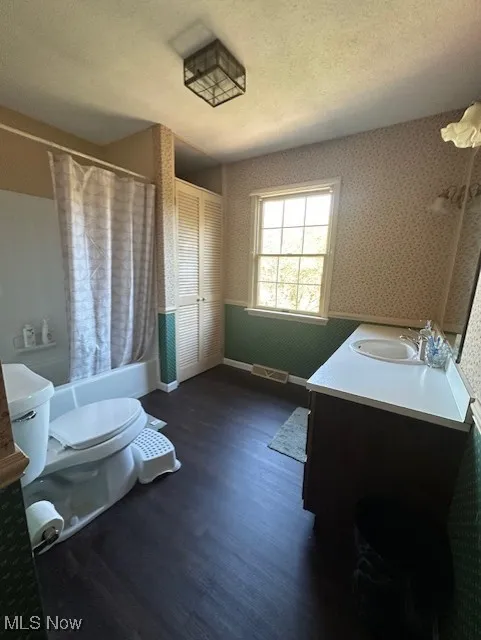 Bathroom with vanity, wallpapered walls, shower / bath combo, dark wood-type flooring, and a textured ceiling