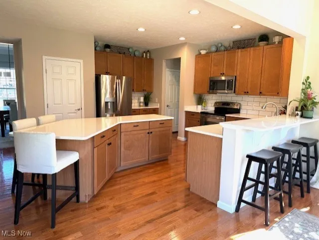 Kitchen with a breakfast bar area, brown cabinetry, stainless steel appliances, decorative backsplash, and recessed lighting