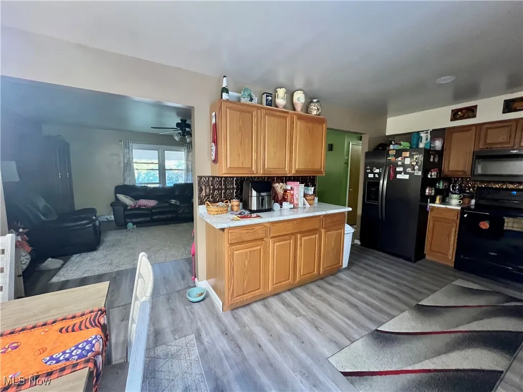 Kitchen with black stainless appliances, light countertops, open floor plan, light wood-style flooring, and decorative backsplash