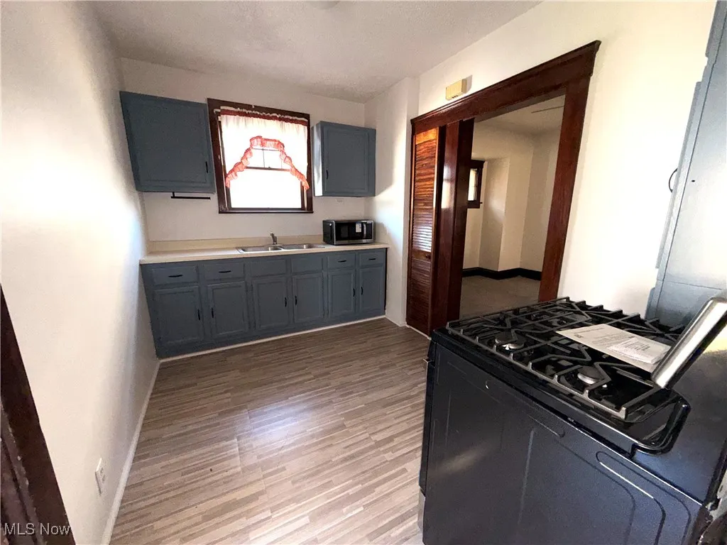 Kitchen with black range with gas stovetop, dark wood-style floors, light countertops, gray cabinets, and stainless steel microwave