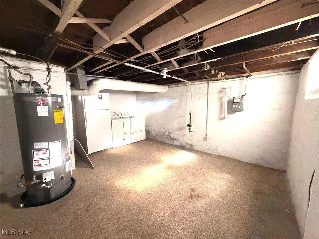 Unfinished basement with water heater and freestanding refrigerator