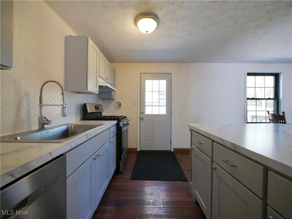 Kitchen featuring appliances with stainless steel finishes, light countertops, gray cabinets, dark wood finished floors, and a textured ceiling