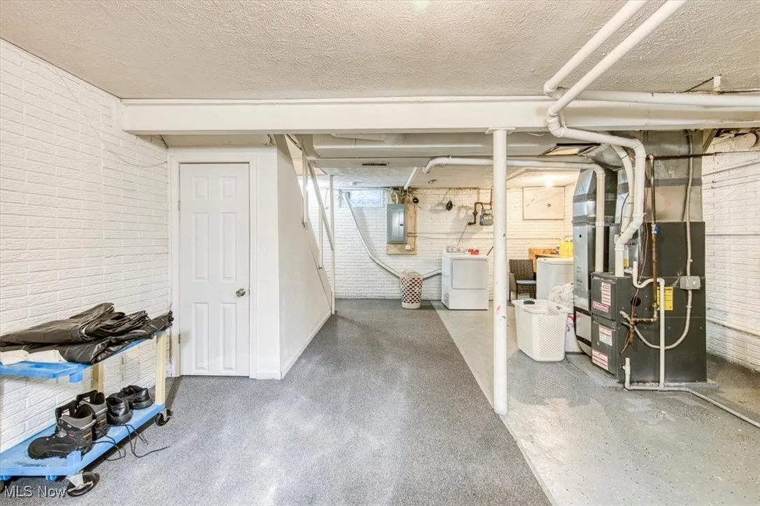 Below grade area featuring brick wall, a textured ceiling, washer / clothes dryer, heating unit, and electric panel