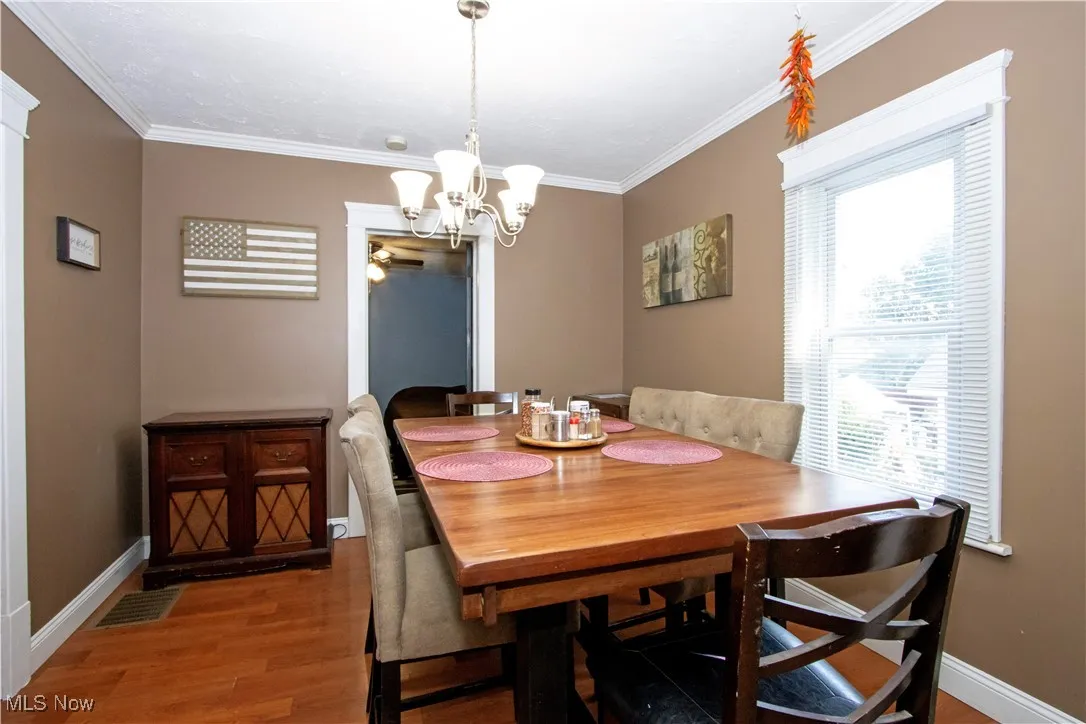 Dining area with wood finished floors, crown molding, and a chandelier