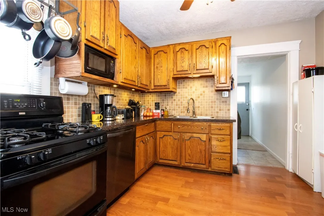 Kitchen featuring black appliances, brown cabinets, backsplash, light wood-style floors, and a textured ceiling