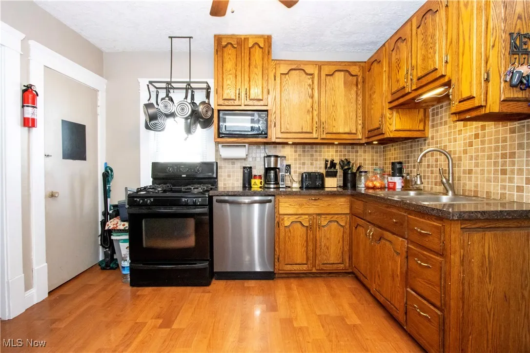 Kitchen with brown cabinets, backsplash, black appliances, light wood finished floors, and a textured ceiling