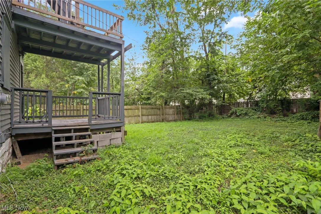 Fenced backyard featuring a wooden deck, stairway, and view of scattered trees