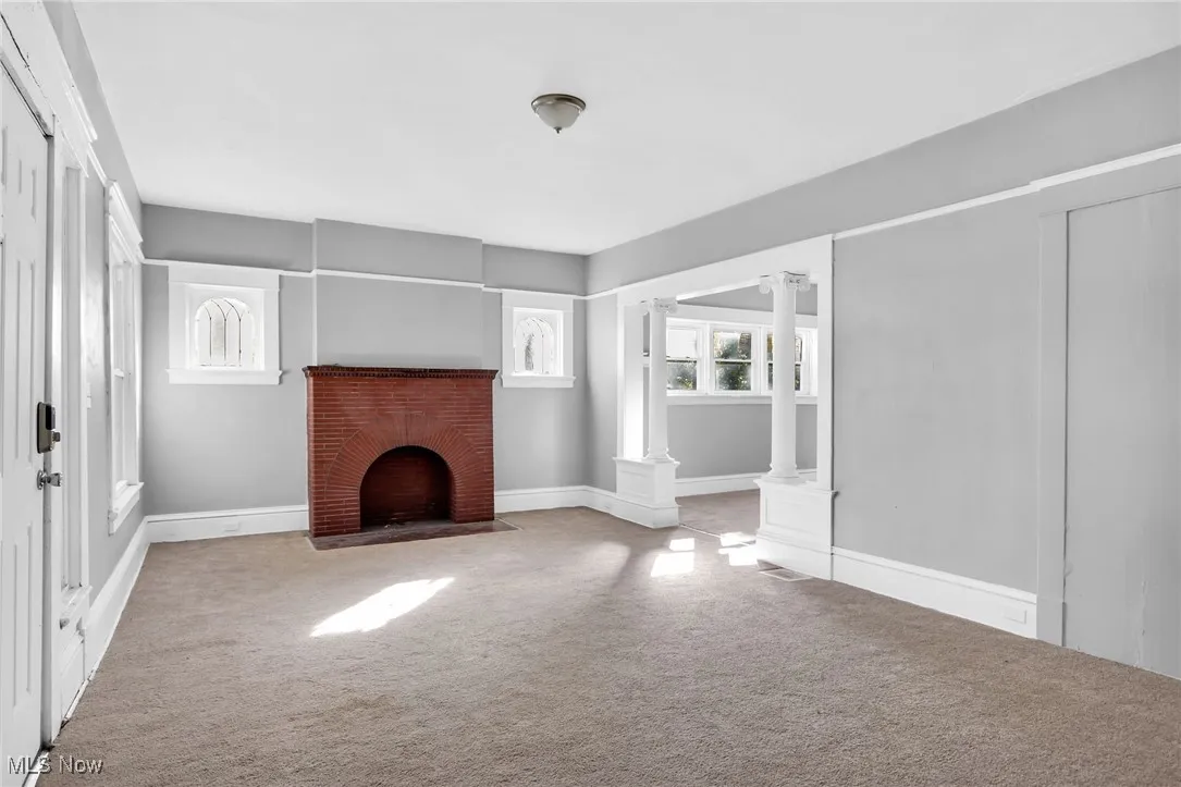 Unfurnished living room featuring decorative columns, carpet floors, and a fireplace