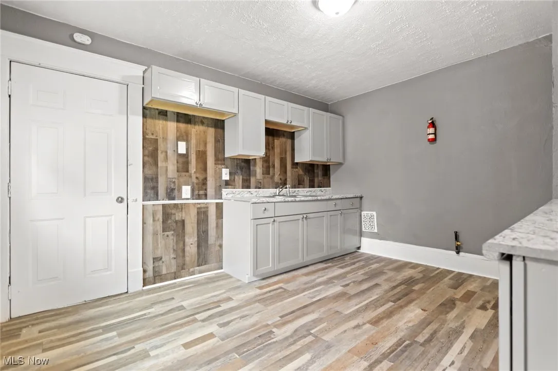 Kitchen with light wood-style floors, wooden walls, a textured ceiling, and light stone countertops
