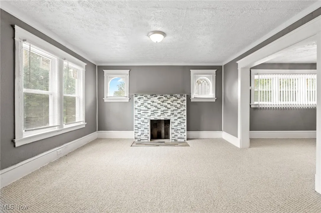 Unfurnished living room featuring carpet floors, a textured ceiling, and a tile fireplace