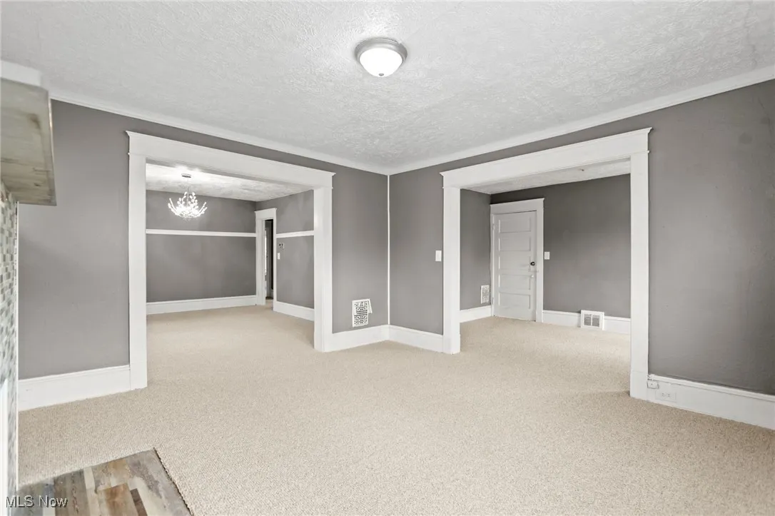 Carpeted spare room featuring a textured ceiling, a chandelier, and crown molding