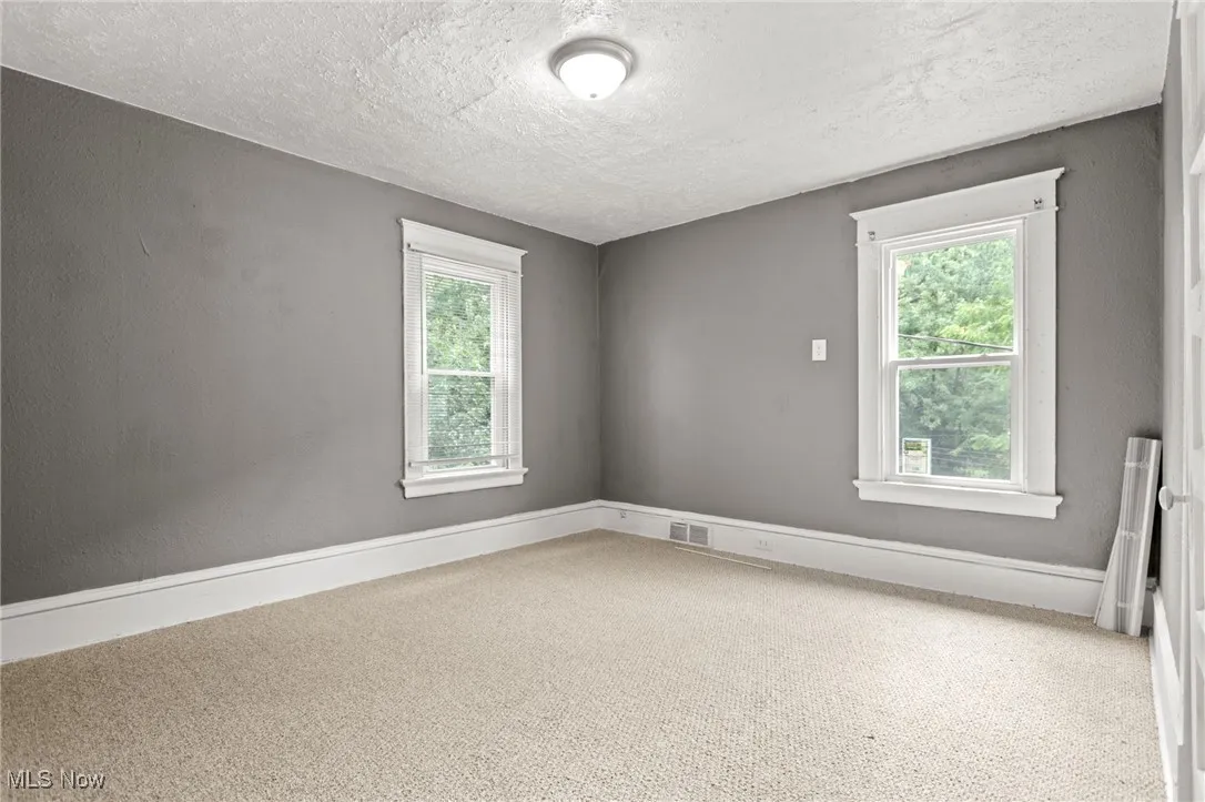 Empty room featuring a textured ceiling, carpet flooring, and radiator heating unit