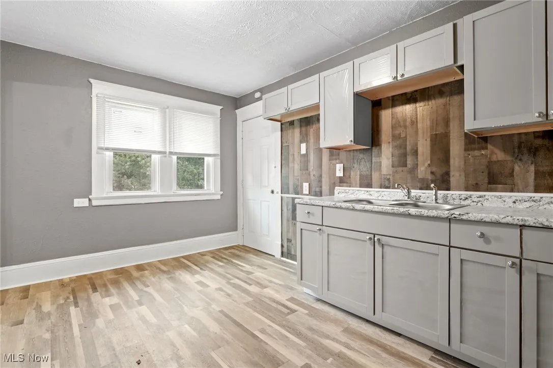 Kitchen with gray cabinetry, light wood-type flooring, a textured ceiling, and light stone counters