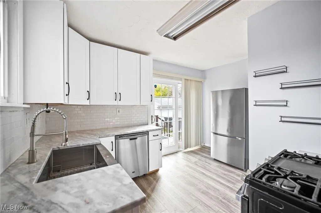 Kitchen with stainless steel appliances, white cabinetry, backsplash, light wood-style floors, and light stone countertops