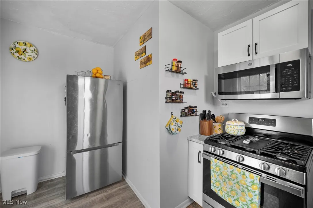 Kitchen with appliances with stainless steel finishes, white cabinets, light wood-type flooring, and light countertops