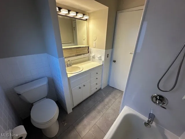 Full bath featuring tile walls, vanity, light tile patterned floors, a wainscoted wall, and shower / washtub combination