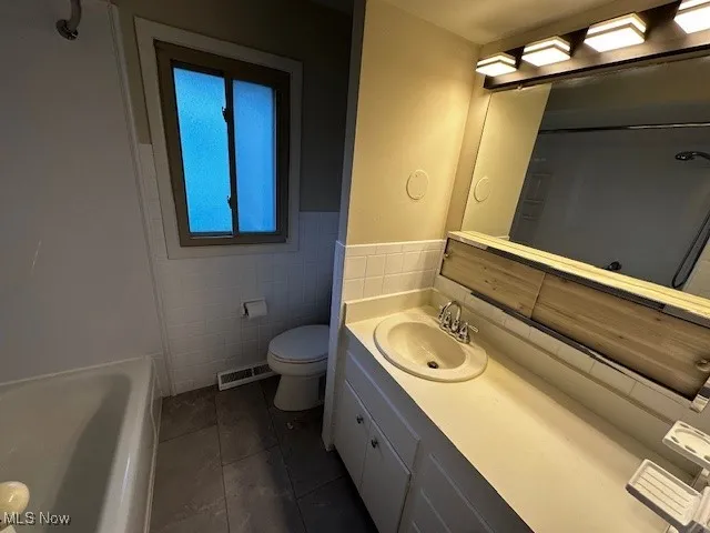Full bath with vanity, dark tile patterned flooring, and tile walls