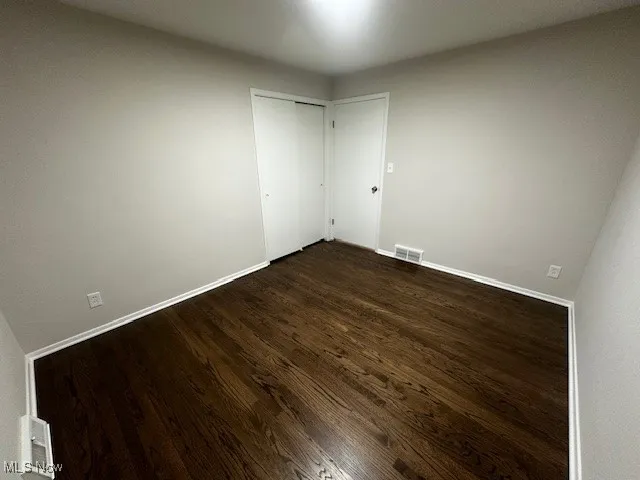 Unfurnished bedroom featuring dark wood-style flooring and a closet