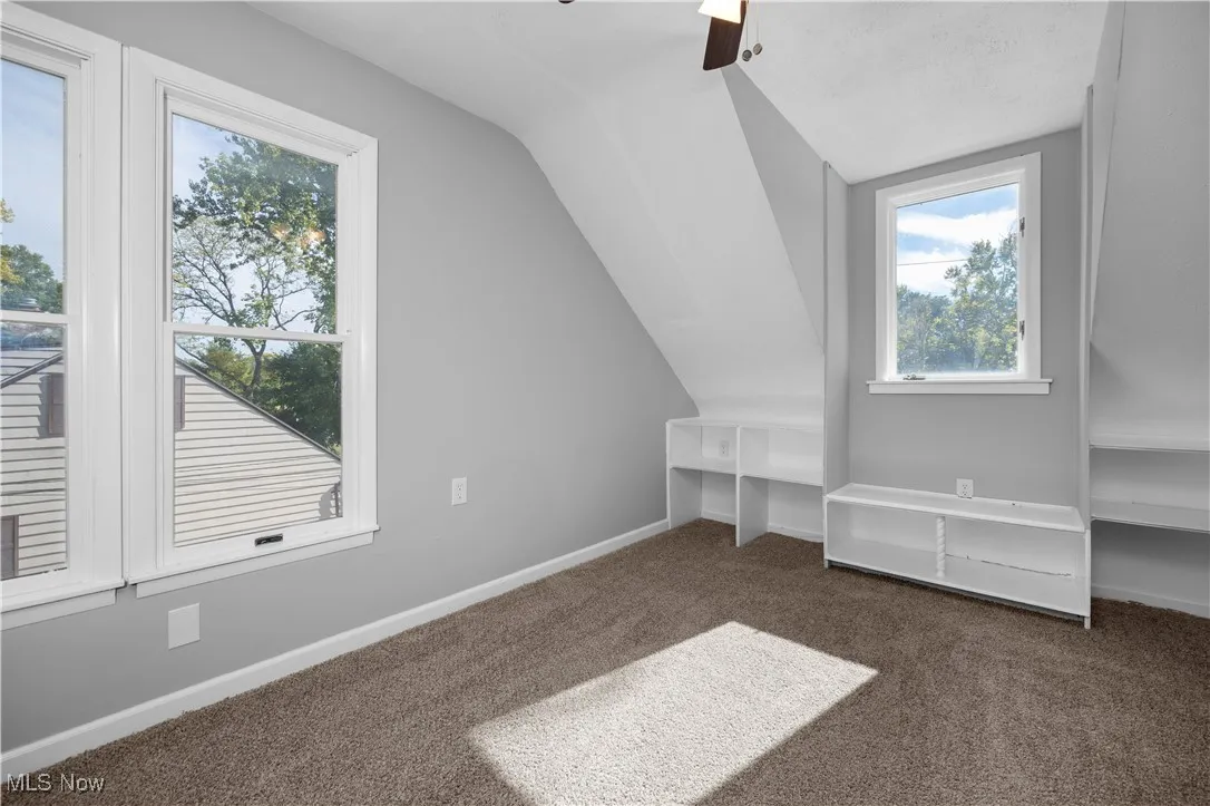Bonus room with dark colored carpet, lofted ceiling, and a ceiling fan