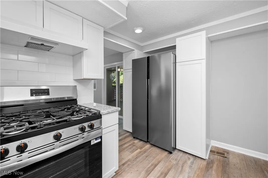 Kitchen featuring appliances with stainless steel finishes, light wood finished floors, a textured ceiling, white cabinetry, and under cabinet range hood