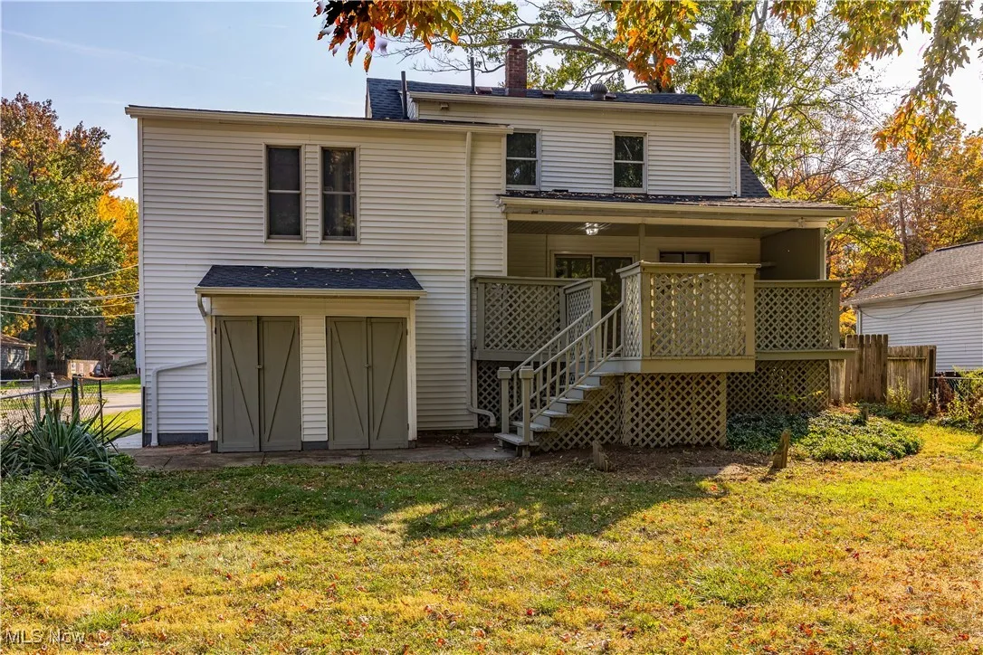 Rear view of property featuring a chimney, stairway, a shingled roof, and a storage unit
