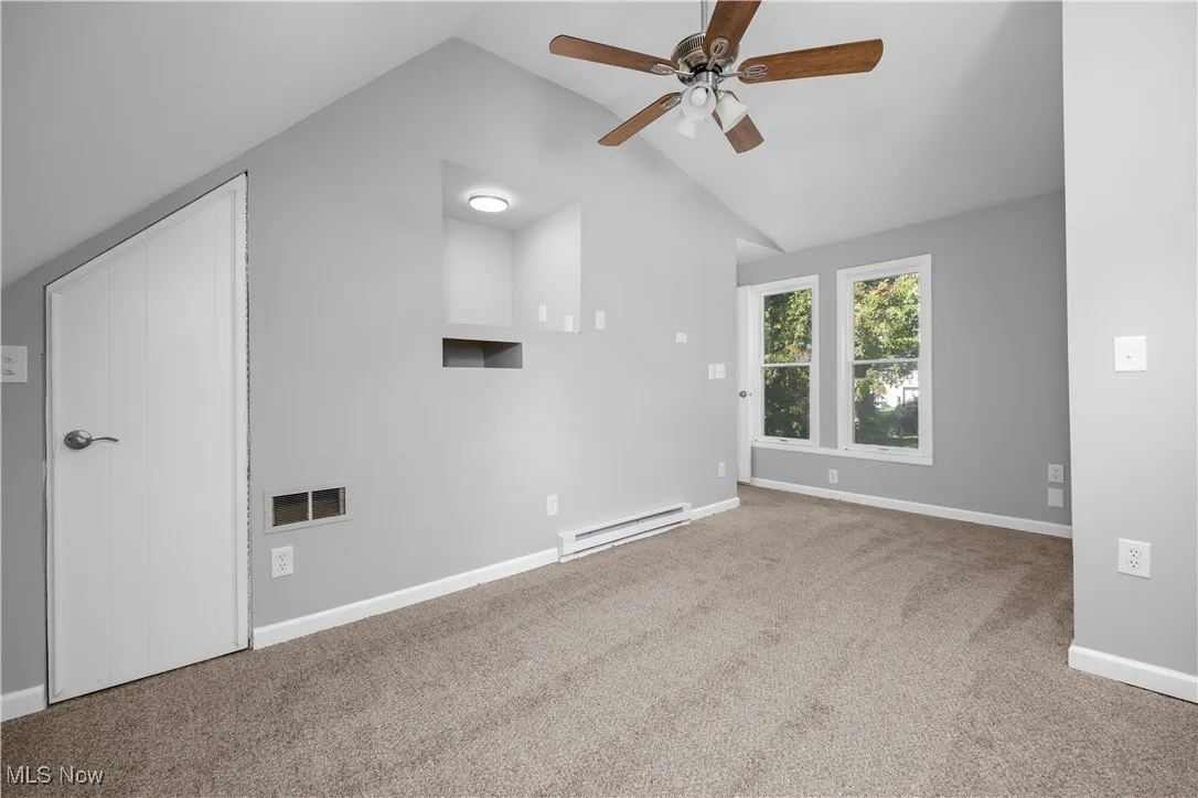 Unfurnished room featuring carpet, baseboard heating, vaulted ceiling, and a ceiling fan