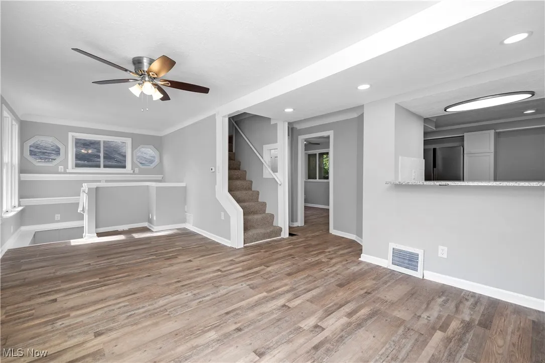 Unfurnished living room with stairway, wood finished floors, a ceiling fan, plenty of natural light, and recessed lighting
