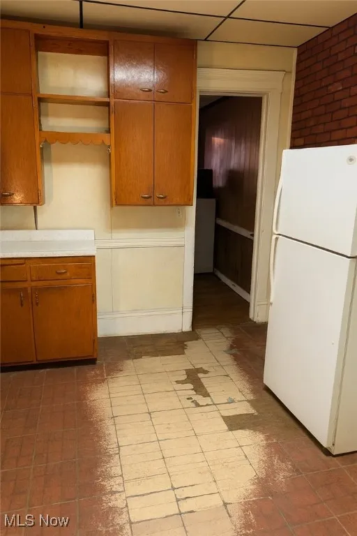Kitchen with freestanding refrigerator, brown cabinetry, and light countertops