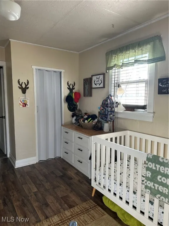 Bedroom featuring dark wood-type flooring, a closet, a textured ceiling, and a nursery area