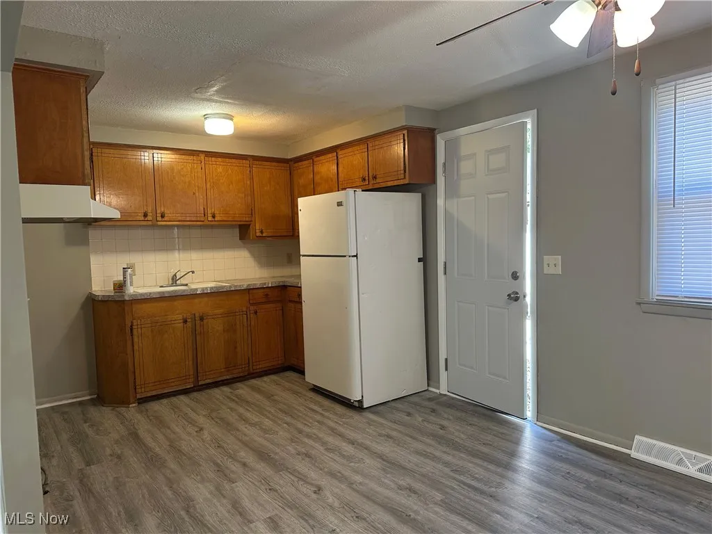 Kitchen featuring brown cabinets, freestanding refrigerator, tasteful backsplash, dark wood-type flooring, and a textured ceiling