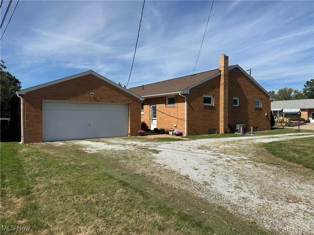 View of side of home featuring brick siding, a chimney, a garage, driveway, and a yard
