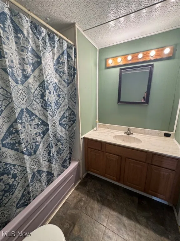 Bathroom with vanity, a textured ceiling, shower / bathtub combination with curtain, and dark tile patterned flooring
