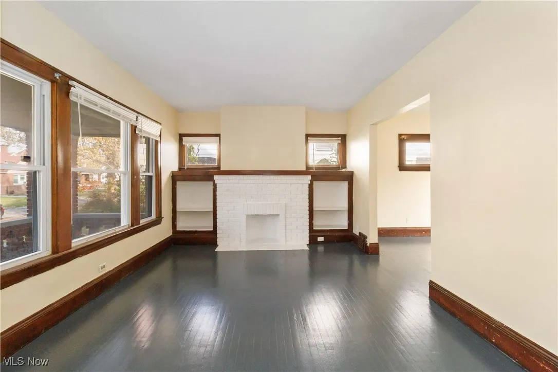 Unfurnished living room with dark wood-style flooring, healthy amount of natural light, and a brick fireplace