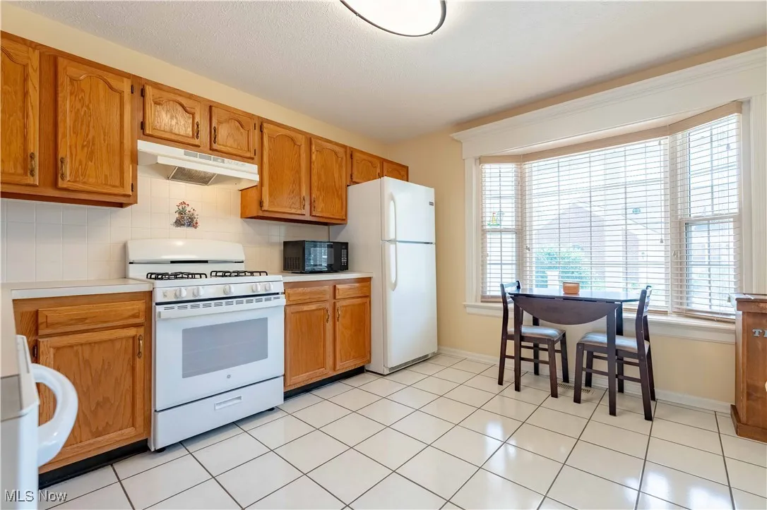 Kitchen with white appliances, under cabinet range hood, light countertops, brown cabinets, and decorative backsplash