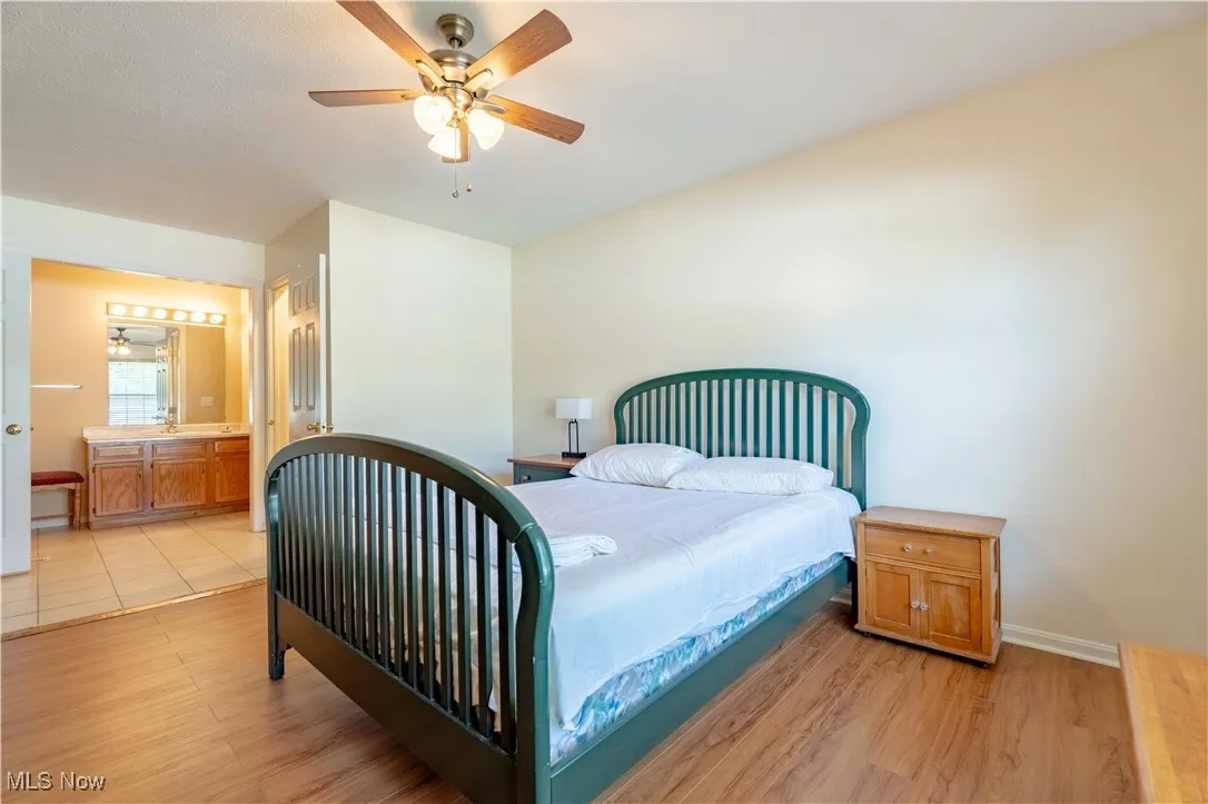 Bedroom with light wood-type flooring, ceiling fan, and ensuite bath