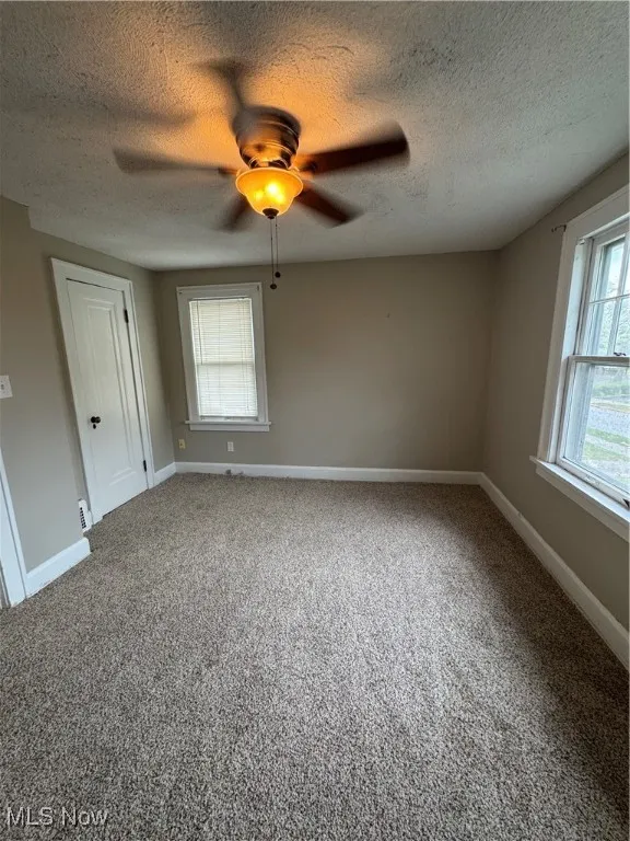 Unfurnished room featuring carpet, a textured ceiling, and a ceiling fan