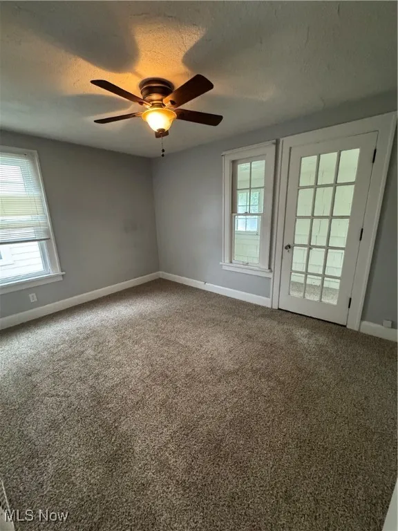 Empty room with a textured ceiling, carpet floors, and a ceiling fan