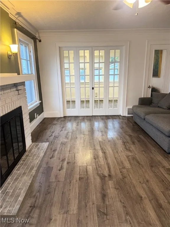 Unfurnished living room featuring a fireplace, crown molding, dark wood-style flooring, a textured ceiling, and a ceiling fan