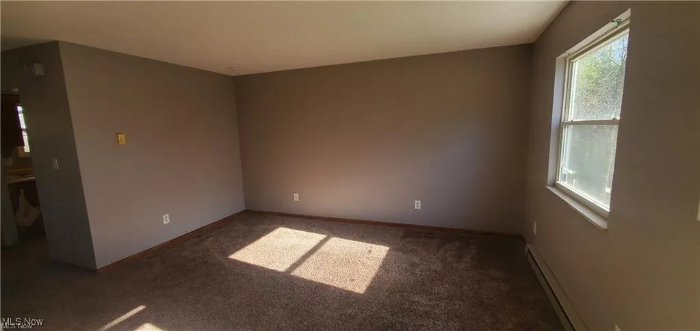 Empty room featuring carpet and a baseboard heating unit